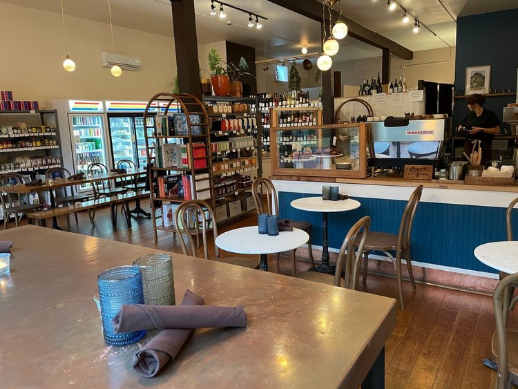 Restaurant/marketinterior with a counter, a table for eating and a shelf of wines in thebackground