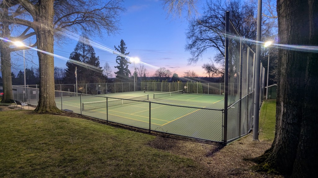 Tennis court at night under the lights with trees on the sides